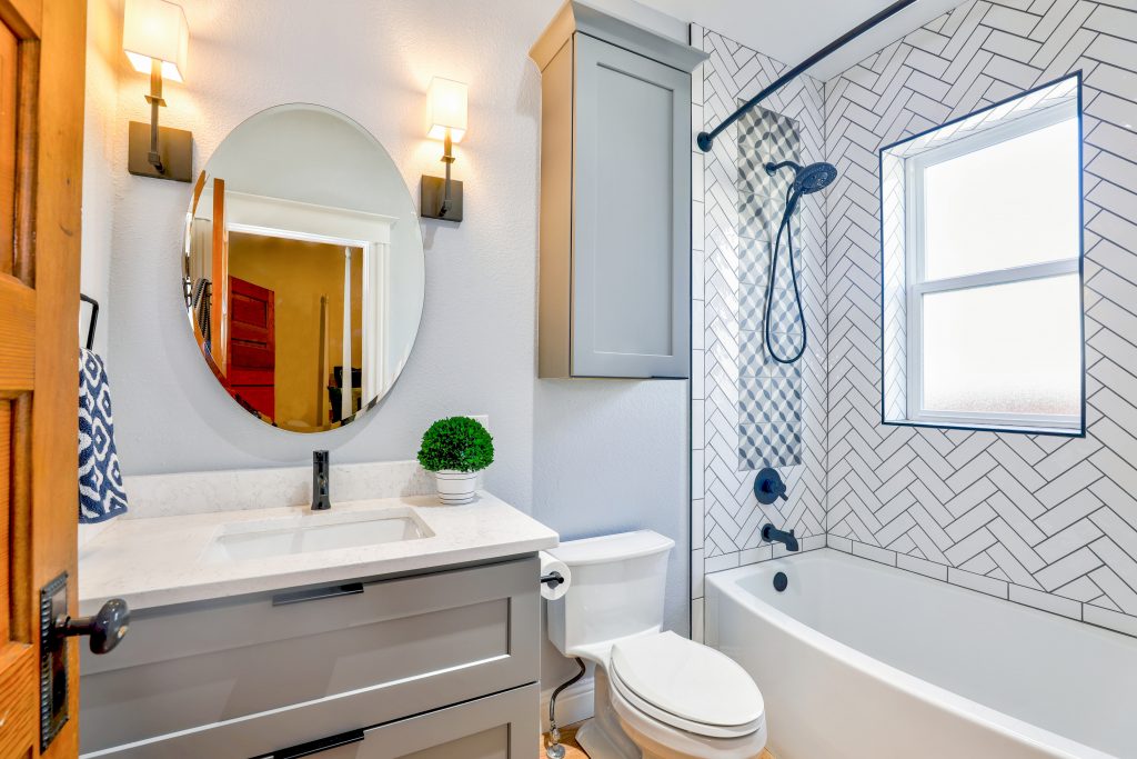 bathroom photo with a grey cabinet, a round mirror and zig zag tile in the shower